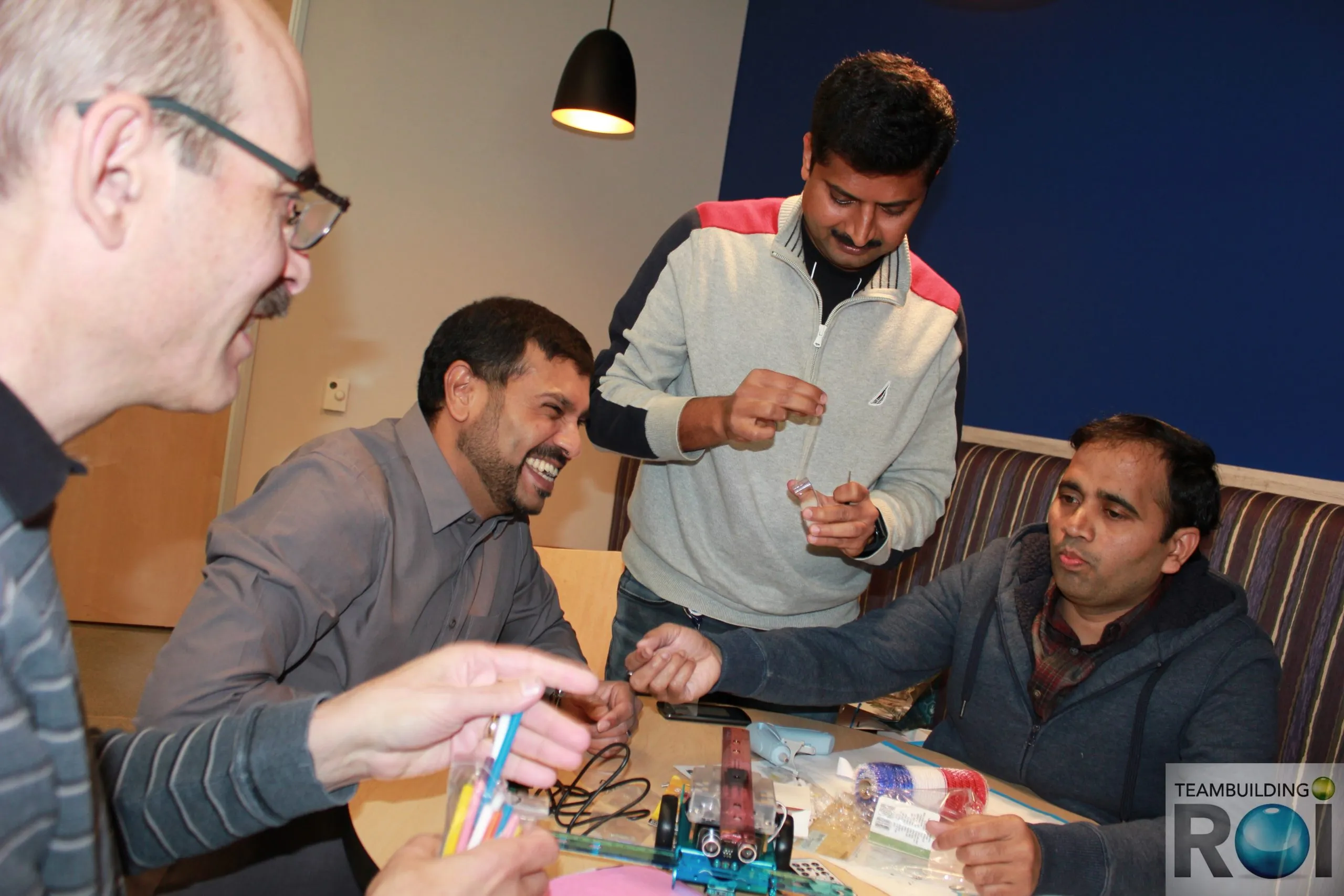 A group of men smiling and assembling a small robot with colorful components at a table during the Robot Rally event